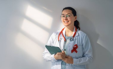 Female doctor on grey wall background. Raising knowledge on people living with tumor illness. clipart