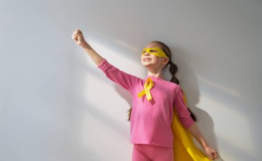 Dünya Çocuk Kanser Günü. Altın kurdeleli süper kahraman kostümlü kız.. 