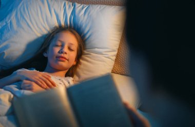 Sevgi dolu bir aile. Güzel genç anne, kızına evde yatakta kitap okuyor..