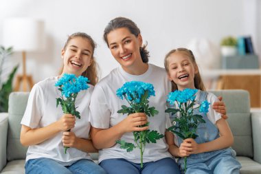 Anneler Günün kutlu olsun. Çocuklar annelerini tebrik ediyor ve ona çiçek veriyorlar. Anne ve kızlar gülümsüyor ve sarılıyorlar. Aile tatili ve birliktelik.