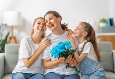 Anneler Günün kutlu olsun. Çocuklar annelerini tebrik ediyor ve ona çiçek veriyorlar. Anne ve kızlar gülümsüyor ve sarılıyorlar. Aile tatili ve birliktelik.