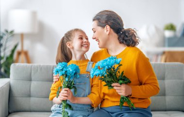 Mutlu kadınlar günü. Çocuk kızı annemi tebrik ediyor ve ona çiçek veriyor. Anne ve kız gülümsüyor ve sarılıyorlar. Aile tatili ve birliktelik.