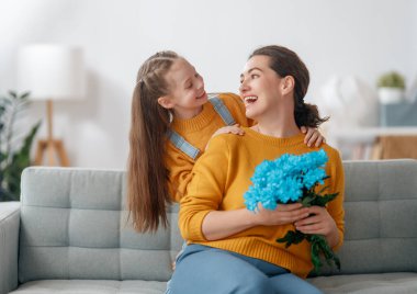 Mutlu kadınlar günü. Çocuk kızı annemi tebrik ediyor ve ona çiçek veriyor. Anne ve kız gülümsüyor ve sarılıyorlar. Aile tatili ve birliktelik.