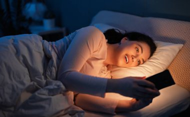 Mutlu, sıradan, güzel bir kadın evdeki yatakta telefon kullanıyor..