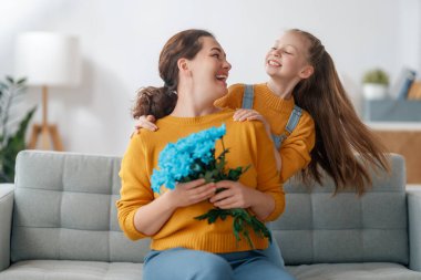 Mutlu kadınlar günü. Çocuk kızı annemi tebrik ediyor ve ona çiçek veriyor. Anne ve kız gülümsüyor ve sarılıyorlar. Aile tatili ve birliktelik.
