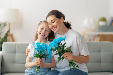Mutlu kadınlar günü. Çocuk kızı annemi tebrik ediyor ve ona çiçek veriyor. Anne ve kız gülümsüyor ve sarılıyorlar. Aile tatili ve birliktelik.