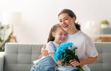 Mutlu kadınlar günü. Çocuk kızı annemi tebrik ediyor ve ona çiçek veriyor. Anne ve kız gülümsüyor ve sarılıyorlar. Aile tatili ve birliktelik.