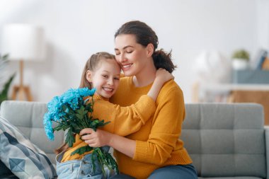 Mutlu kadınlar günü. Çocuk kızı annemi tebrik ediyor ve ona çiçek veriyor. Anne ve kız gülümsüyor ve sarılıyorlar. Aile tatili ve birliktelik.