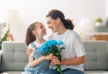 Mutlu kadınlar günü. Çocuk kızı annemi tebrik ediyor ve ona çiçek veriyor. Anne ve kız gülümsüyor ve sarılıyorlar. Aile tatili ve birliktelik.