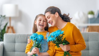Mutlu kadınlar günü. Çocuk kızı annemi tebrik ediyor ve ona çiçek veriyor. Anne ve kız gülümsüyor ve sarılıyorlar. Aile tatili ve birliktelik.