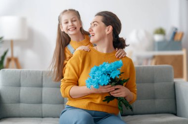 Mutlu kadınlar günü. Çocuk kızı annemi tebrik ediyor ve ona çiçek veriyor. Anne ve kız gülümsüyor ve sarılıyorlar. Aile tatili ve birliktelik.