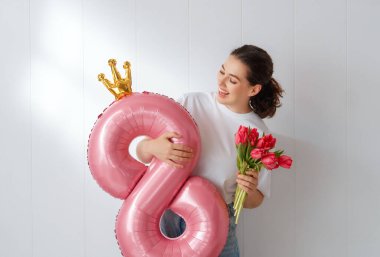 Kırmızı çiçekli güzel bir kadın ve beyaz duvarda sekiz şeklinde bir balon..