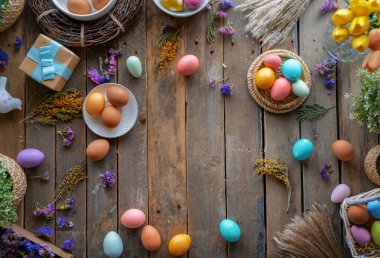 Paskalya tatili geçmişi. Ahşap masada renkli yumurtalar ve çiçekler. Üst görünüm