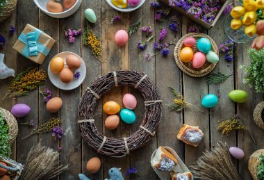 Paskalya tatili geçmişi. Ahşap masada renkli yumurtalar ve çiçekler. Üst görünüm
