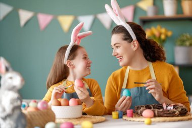 Anne ve kızı yumurta boyuyor. Mutlu aile Paskalya için hazırlanıyor. Tavşan kulağı takan şirin bir kız çocuğu..