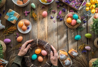 Paskalya tatili geçmişi. Ahşap masada renkli yumurtalar ve çiçekler. Üst görünüm