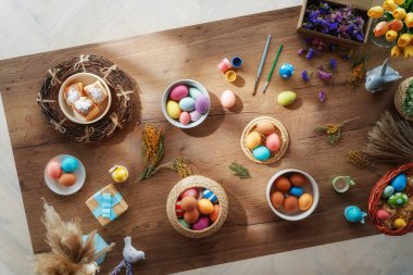 Paskalya tatili geçmişi. Ahşap masada renkli yumurtalar ve çiçekler. Üst görünüm