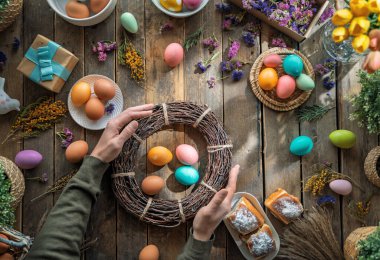 Paskalya tatili geçmişi. Ahşap masada renkli yumurtalar ve çiçekler. Üst görünüm