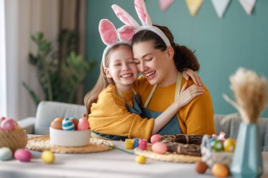 Anne ve kızı yumurta boyuyor. Mutlu aile Paskalya için hazırlanıyor. Tavşan kulağı takan şirin bir kız çocuğu..