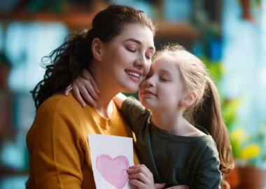 Anneler Günün kutlu olsun. Çocuk kızı annemi tebrik ediyor ve ona kartpostal veriyor. Anne ve kız gülümsüyor ve sarılıyorlar. Aile tatili ve birliktelik.