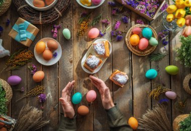 Paskalya tatili geçmişi. Ahşap masada renkli yumurtalar ve çiçekler. Üst görünüm