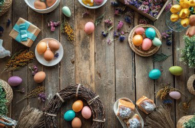 Paskalya tatili geçmişi. Ahşap masada renkli yumurtalar ve çiçekler. Üst görünüm