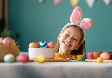 Yumurta boyayan güzel bir çocuk. Mutlu aile Paskalya için hazırlanıyor. Sevimli küçük kız tavşan kulağı takıyor..  