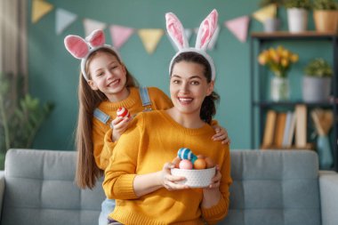 İyi tatiller! Anne ve kızı yumurta boyuyor. Paskalyayı kutlayan aile. Sevimli küçük kız tavşan kulağı takıyor..