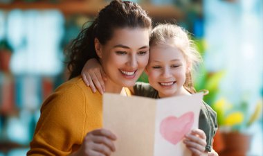 Anneler Günün kutlu olsun. Çocuk kızı annemi tebrik ediyor ve ona kartpostal veriyor. Anne ve kız gülümsüyor ve sarılıyorlar. Aile tatili ve birliktelik.