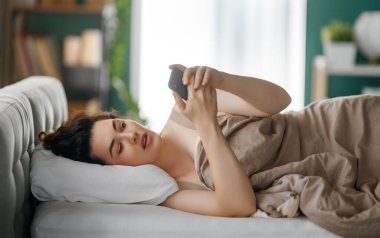 Mutlu, sıradan, güzel bir kadın evdeki yatakta telefon kullanıyor..