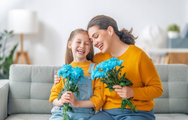 Anneler Günün kutlu olsun. Çocuk kızı annemi tebrik ediyor ve ona çiçek veriyor. Anne ve kız gülümsüyor ve sarılıyorlar. Aile tatili ve birliktelik.