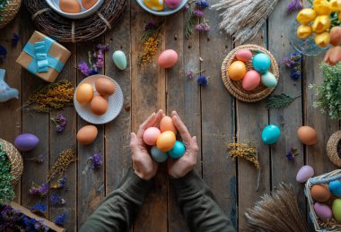Paskalya tatili geçmişi. Ahşap masada renkli yumurtalar ve çiçekler. Üst görünüm
