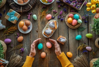 Paskalya tatili geçmişi. Ahşap masada renkli yumurtalar ve çiçekler. Üst görünüm