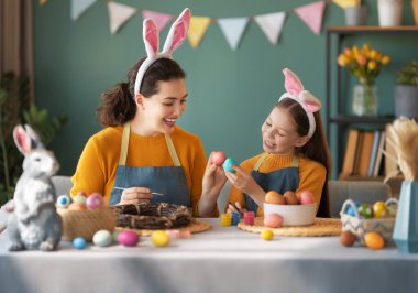 Anne ve kızı yumurta boyuyor. Mutlu aile Paskalya için hazırlanıyor. Tavşan kulağı takan şirin bir kız çocuğu..