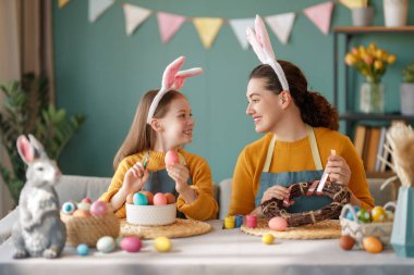 Anne ve kızı yumurta boyuyor. Mutlu aile Paskalya için hazırlanıyor. Tavşan kulağı takan şirin bir kız çocuğu..