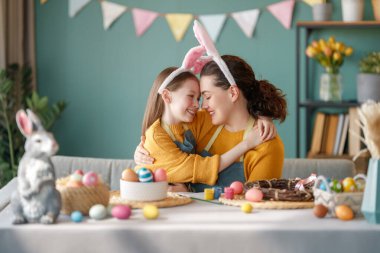 Anne ve kızı yumurta boyuyor. Mutlu aile Paskalya için hazırlanıyor. Tavşan kulağı takan şirin bir kız çocuğu..