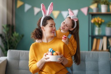İyi tatiller! Anne ve kızı yumurta boyuyor. Paskalyayı kutlayan aile. Sevimli küçük kız tavşan kulağı takıyor..
