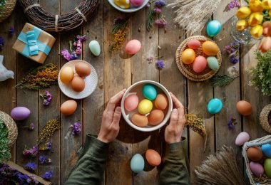 Paskalya tatili geçmişi. Ahşap masada renkli yumurtalar ve çiçekler. Üst görünüm