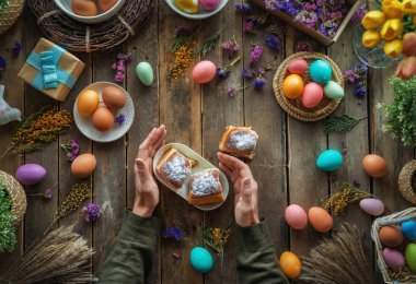 Paskalya tatili geçmişi. Ahşap masada renkli yumurtalar ve çiçekler. Üst görünüm