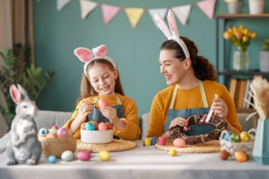 Anne ve kızı yumurta boyuyor. Mutlu aile Paskalya için hazırlanıyor. Tavşan kulağı takan şirin bir kız çocuğu..