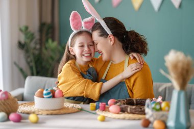 Anne ve kızı yumurta boyuyor. Mutlu aile Paskalya için hazırlanıyor. Tavşan kulağı takan şirin bir kız çocuğu..
