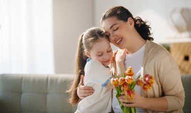 Anneler Günün kutlu olsun. Çocuk kızı annemi tebrik ediyor ve ona çiçek veriyor. Anne ve kız gülümsüyor ve sarılıyorlar. Aile tatili ve birliktelik.