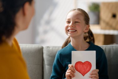 Anneler Günün kutlu olsun. Çocuk kızı annemi tebrik ediyor ve ona kartpostal veriyor. Anne ve kız gülümsüyor ve sarılıyorlar. Aile tatili ve birliktelik.