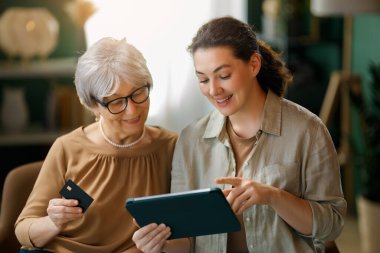 Genç ve yaşlı kadınlar online alışveriş için bilgisayar kullanıyorlar. Kızı evde annesine yardım ediyor..