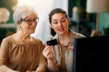 Genç ve yaşlı kadınlar online alışveriş için bilgisayar kullanıyorlar. Kızı evde annesine yardım ediyor..