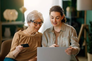 Genç ve yaşlı kadınlar online alışveriş için bilgisayar kullanıyorlar. Kızı evde annesine yardım ediyor..