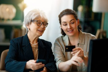 Genç ve yaşlı kadınlar online alışveriş için bilgisayar kullanıyorlar. Kızı evde annesine yardım ediyor..