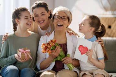 Anneler Günün kutlu olsun! Çocuklar annelerini ve büyükannelerini onlara çiçek veren laleleri kutluyorlar. Büyükanne, anne ve kızlar açık gri arka planda gülümsüyorlar. Aile tatili ve birliktelik