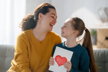 Anneler Günün kutlu olsun. Çocuk kızı annemi tebrik ediyor ve ona kartpostal veriyor. Anne ve kız gülümsüyor ve sarılıyorlar. Aile tatili ve birliktelik.