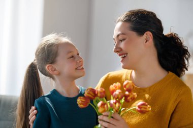 Anneler Günün kutlu olsun. Çocuk kızı annemi tebrik ediyor ve ona çiçek veriyor. Anne ve kız gülümsüyor ve sarılıyorlar. Aile tatili ve birliktelik.